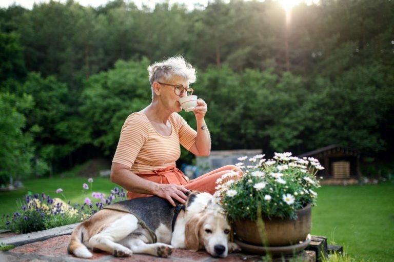 senior woman sitting with a dog and drinking from a cup